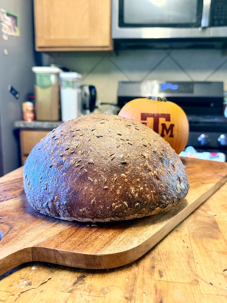 Dark artisan loaf on a wooden board with an autumn pumpkin in the bakery kitchen