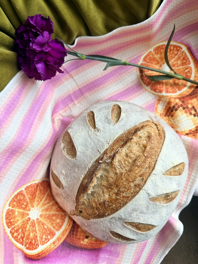 Round artisan sourdough loaf styled with a purple flower and citrus accents