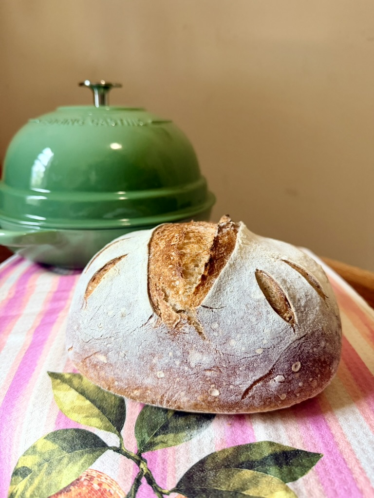 Fresh artisan sourdough loaf beside a green bread cloche