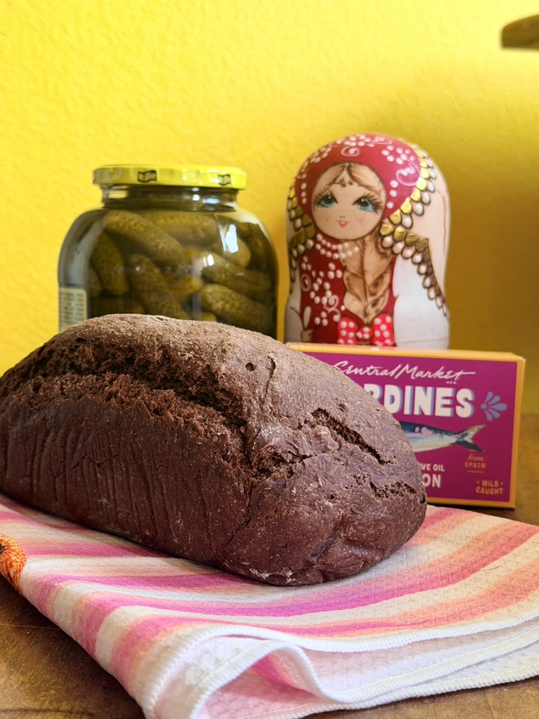 Russian black bread styled with pickles and a painted nesting doll
